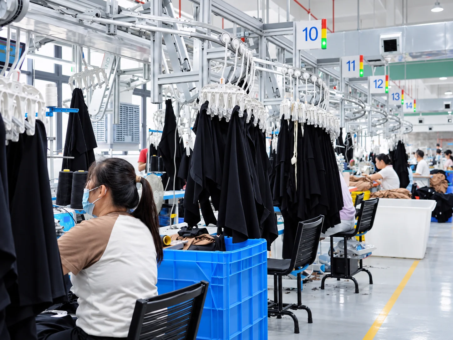 Operators sewing garments at numbered stations along a hanger line.